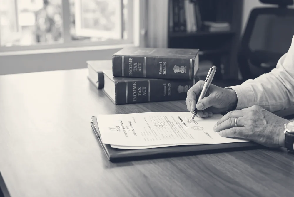 Chartered accountant signing an income tax order beside bound Income Tax Act volumes